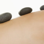 Nude female and warm rock body therapy --- Image by © Tetra Images/Corbis